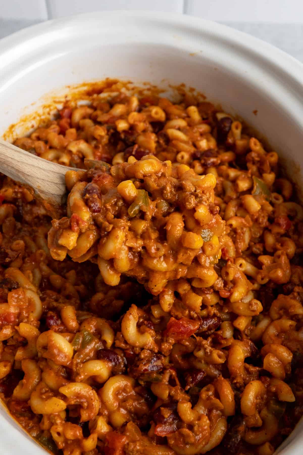 Close-up of chili mac on a wooden spoon over a slow cooker.