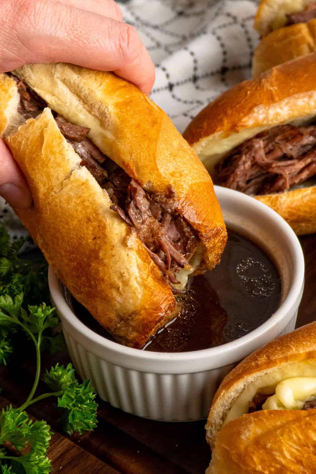 A hand dipping a crock pot French dip sandwich into au jus sauce.