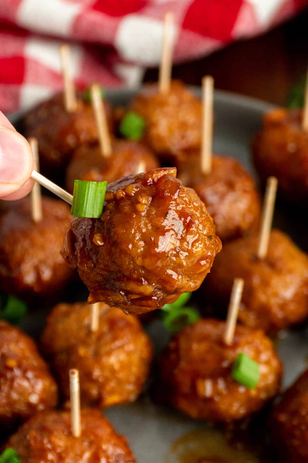 Close up of a hand holding a honey garlic meatballs on a toothpicks.
