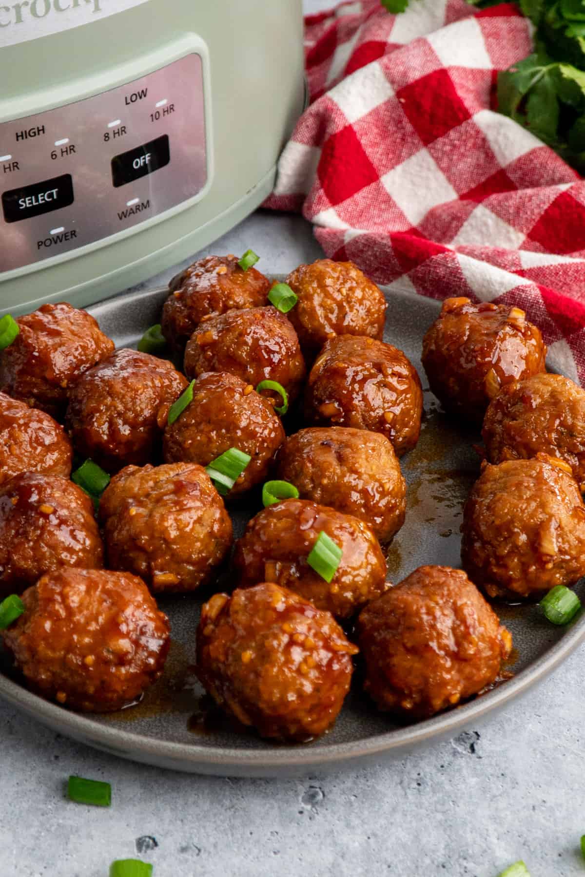 Crock pot honey garlic meatballs on a plate garnished with green onions.