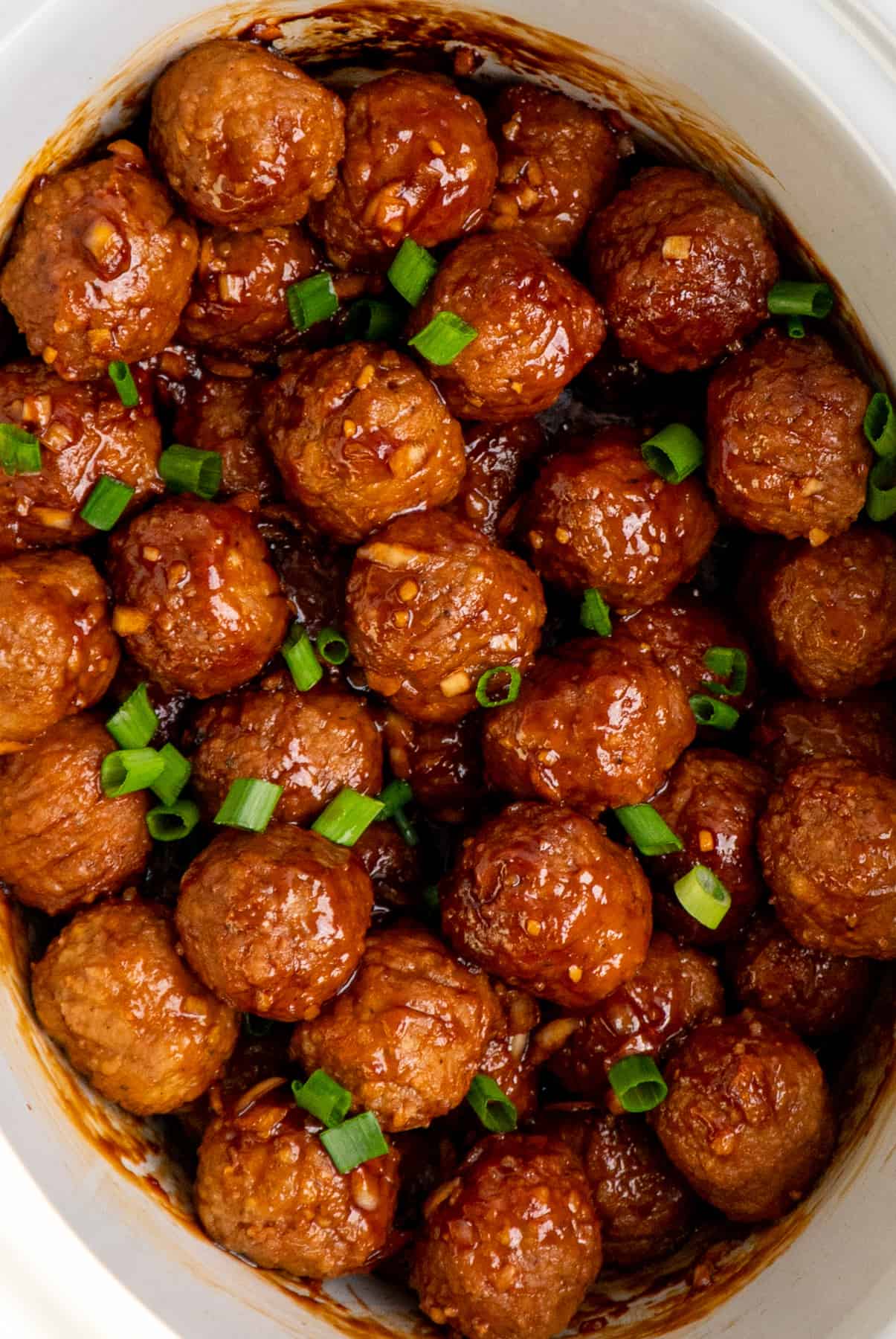 Honey garlic meatballs in a white slow cooker garnished with green onions.