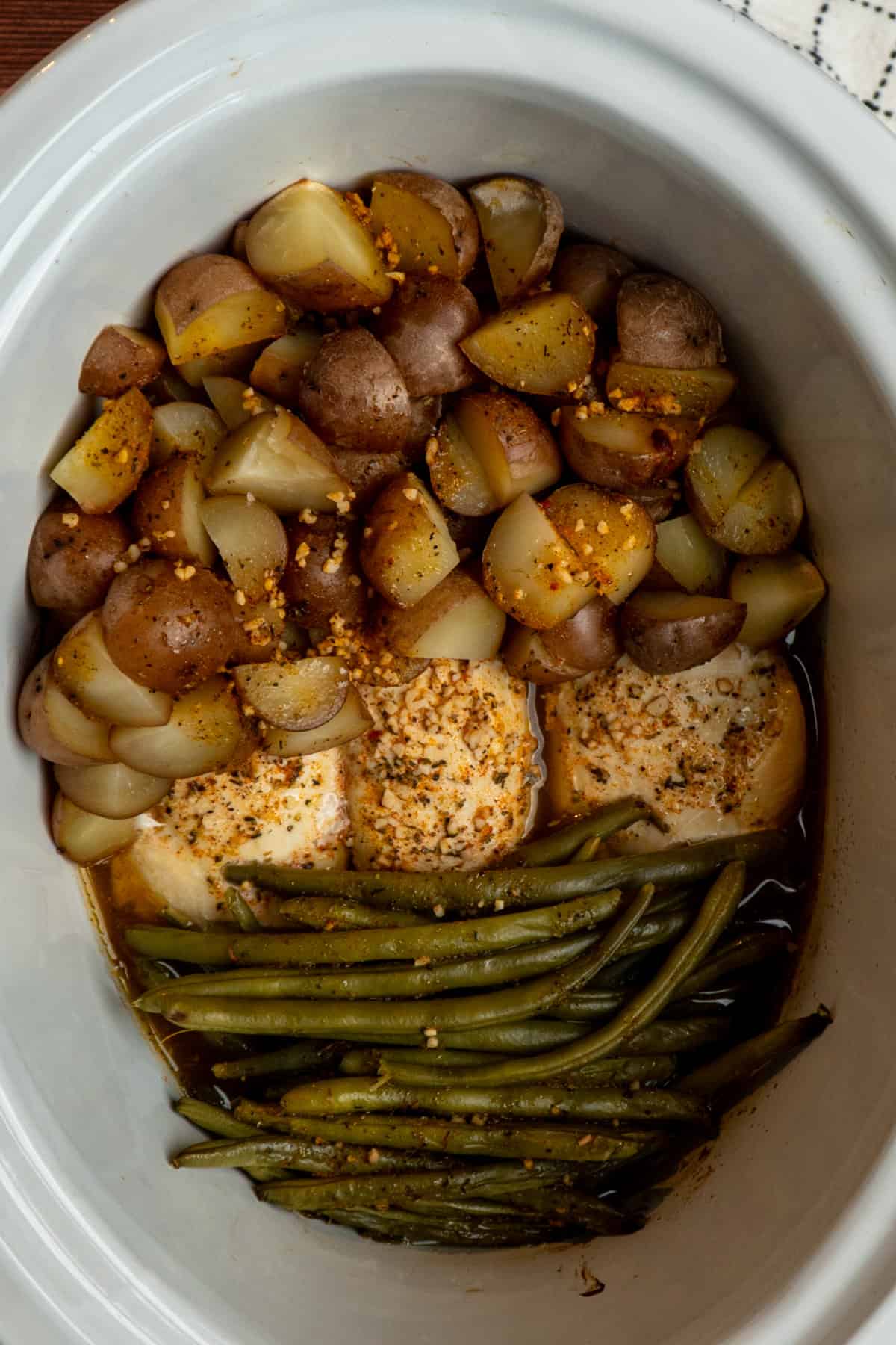 Chicken, potatoes and green beans that have been cooked in a white slow cooker.