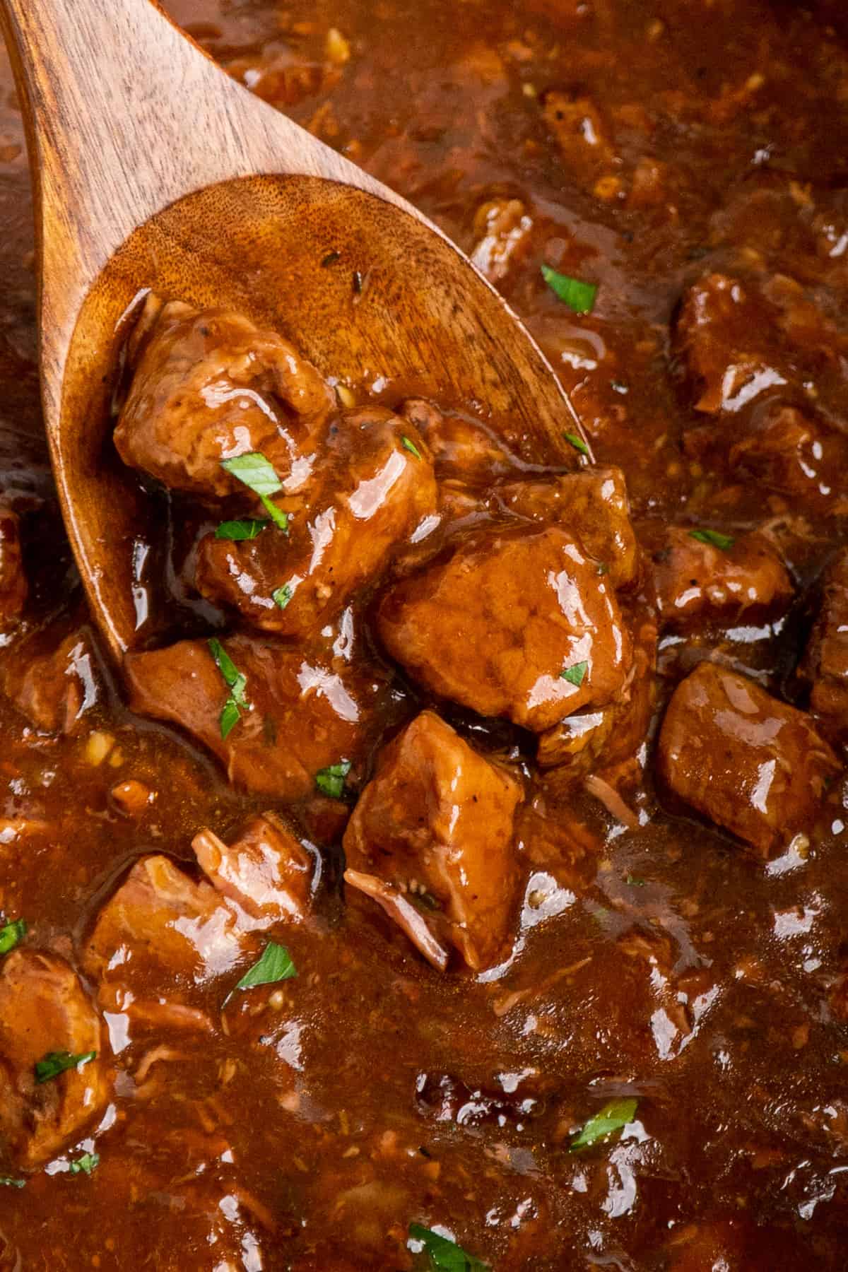 A wooden spoon scooping beef tips and gravin in a slow cooker.