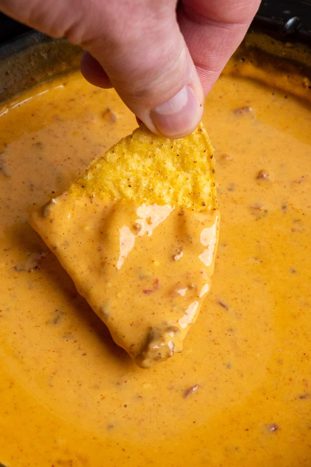 A hand dipping a tortilla chip into Crock Pot chili cheese dip.