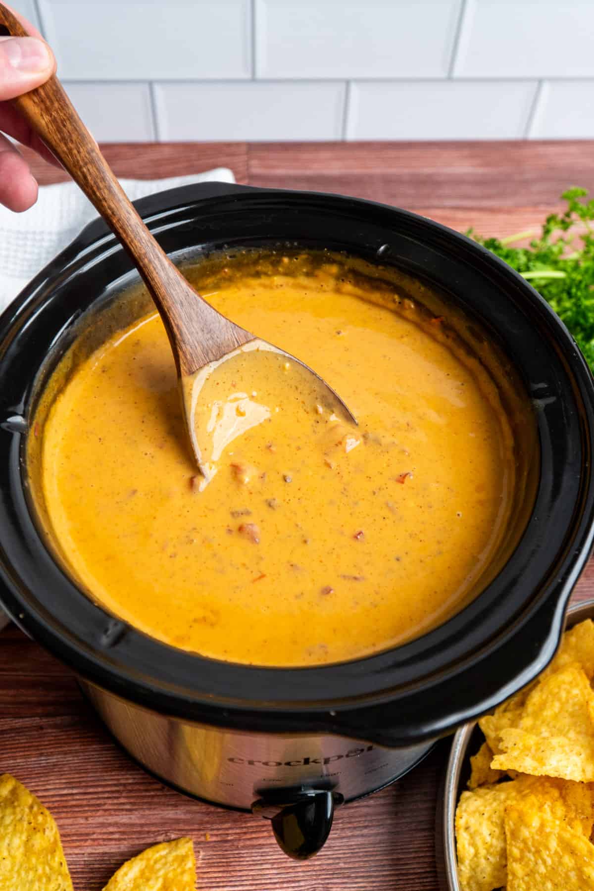 A wooden spoon stirring chili cheese dip.