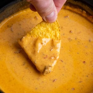 A hand dipping a tortilla chip into Crock Pot chili cheese dip.