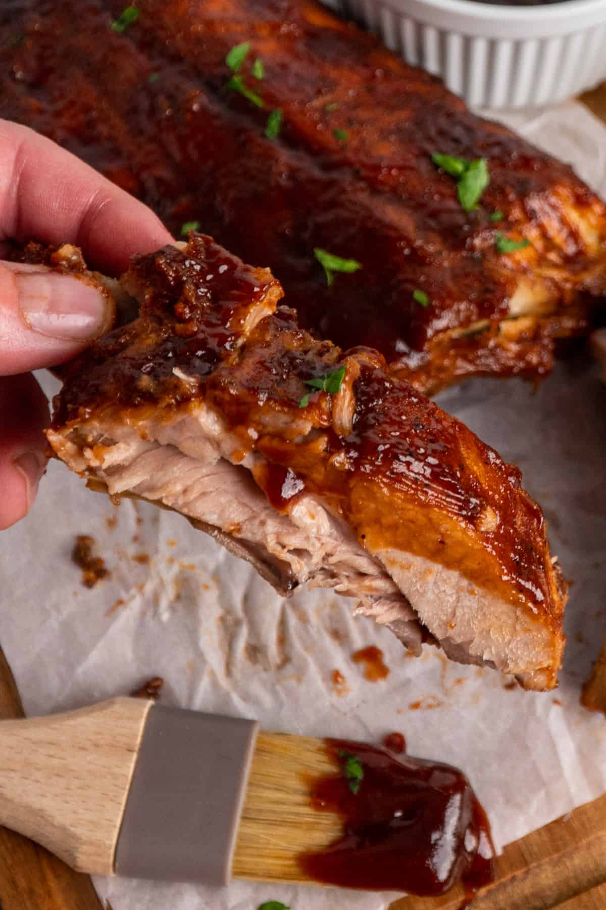 A hand holding a pork rib with bbq sauce on it.