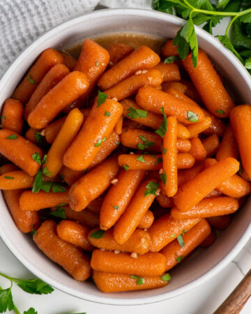 A white bowl of crock pot honey glazed carrots garnished with parsley.