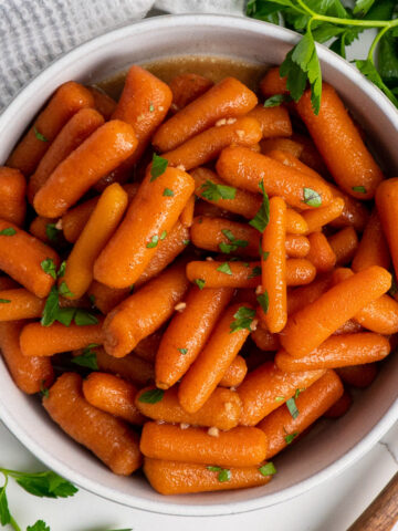 A white bowl of crock pot honey glazed carrots garnished with parsley.