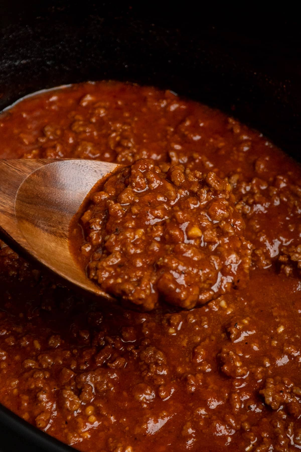 A woodend spoon with a scoop of hot dog chili from a crock pot.