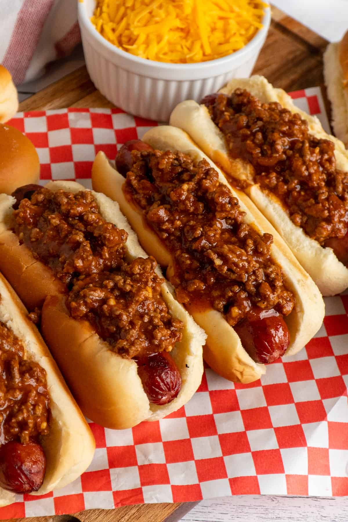 Four hot dogs on a wood cutting board and topped with hot dog chili.