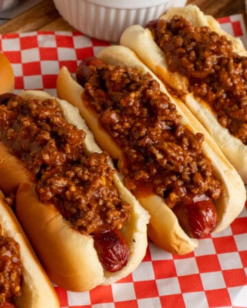 Four hot dogs on a wood cutting board and topped with hot dog chili.