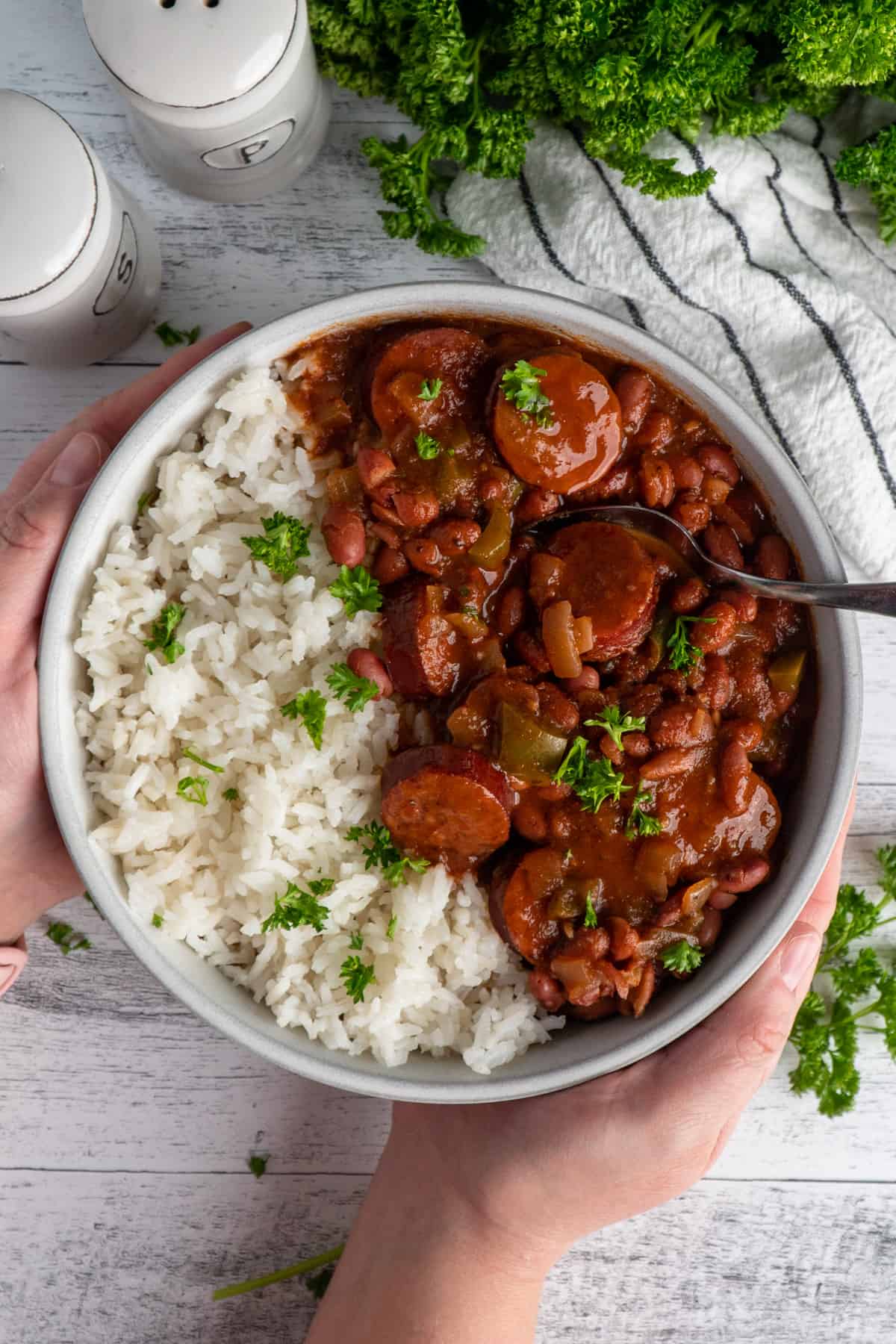 Hands holding a bowl of red beans and rice garnished with parsley.