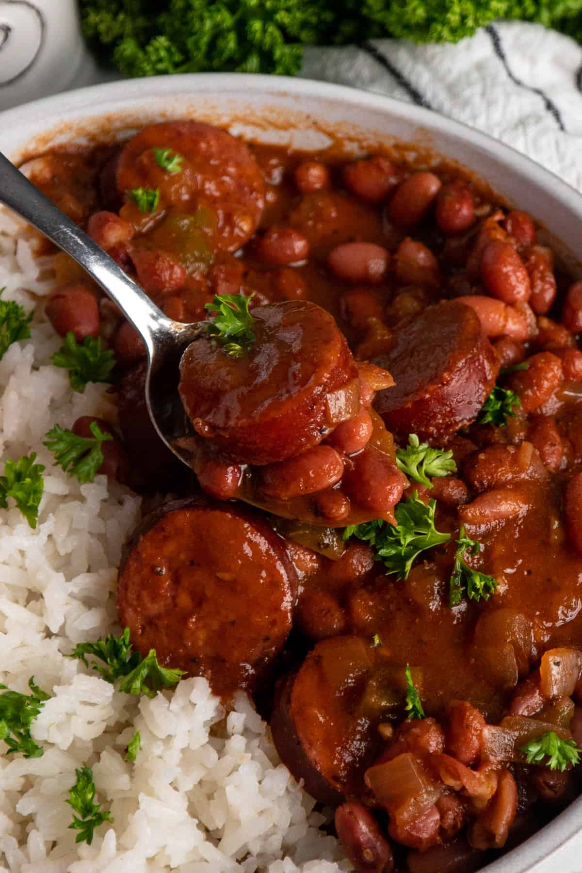 A spoon with a bite of creole beans and sausage with a side of rice.