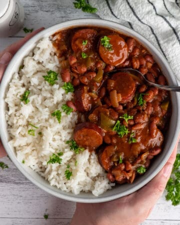 Hands holding a bowl of red beans and rice garnished with parsley.
