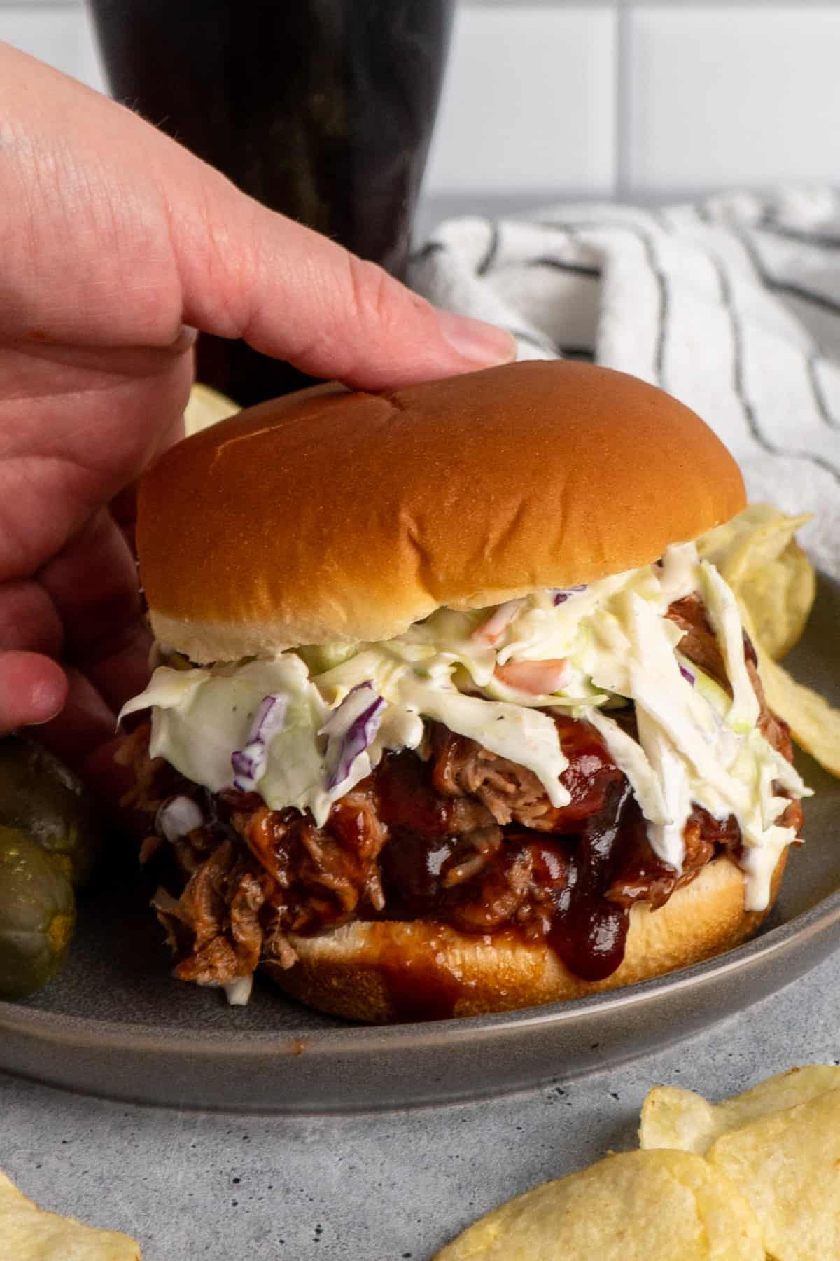 A hand holding a slow cooker bbq pulled pork sandwich.