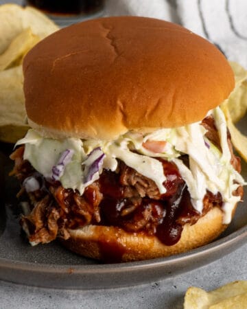 BBQ pulled pork on a bun with coleslaw on a grey plate with chips.