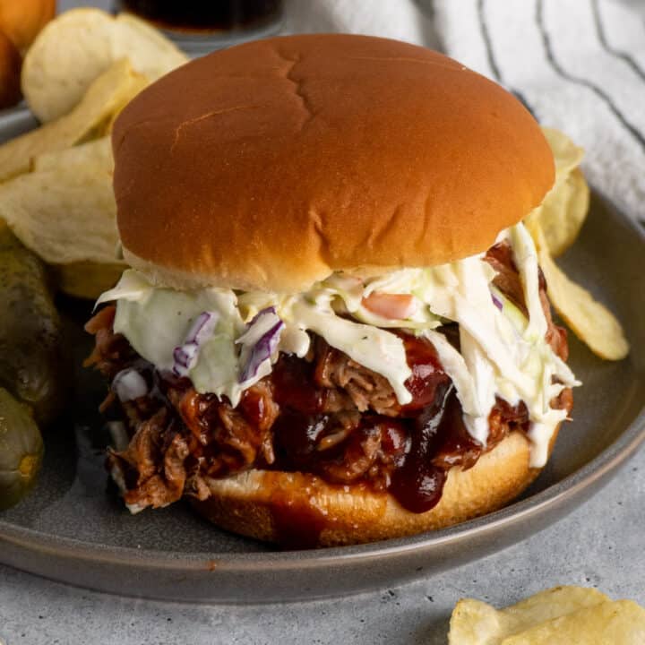 BBQ pulled pork on a bun with coleslaw on a grey plate with chips.