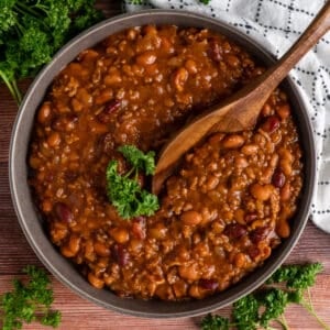 Slow cooker cowboy beans in a bowl with a wooden spoon.