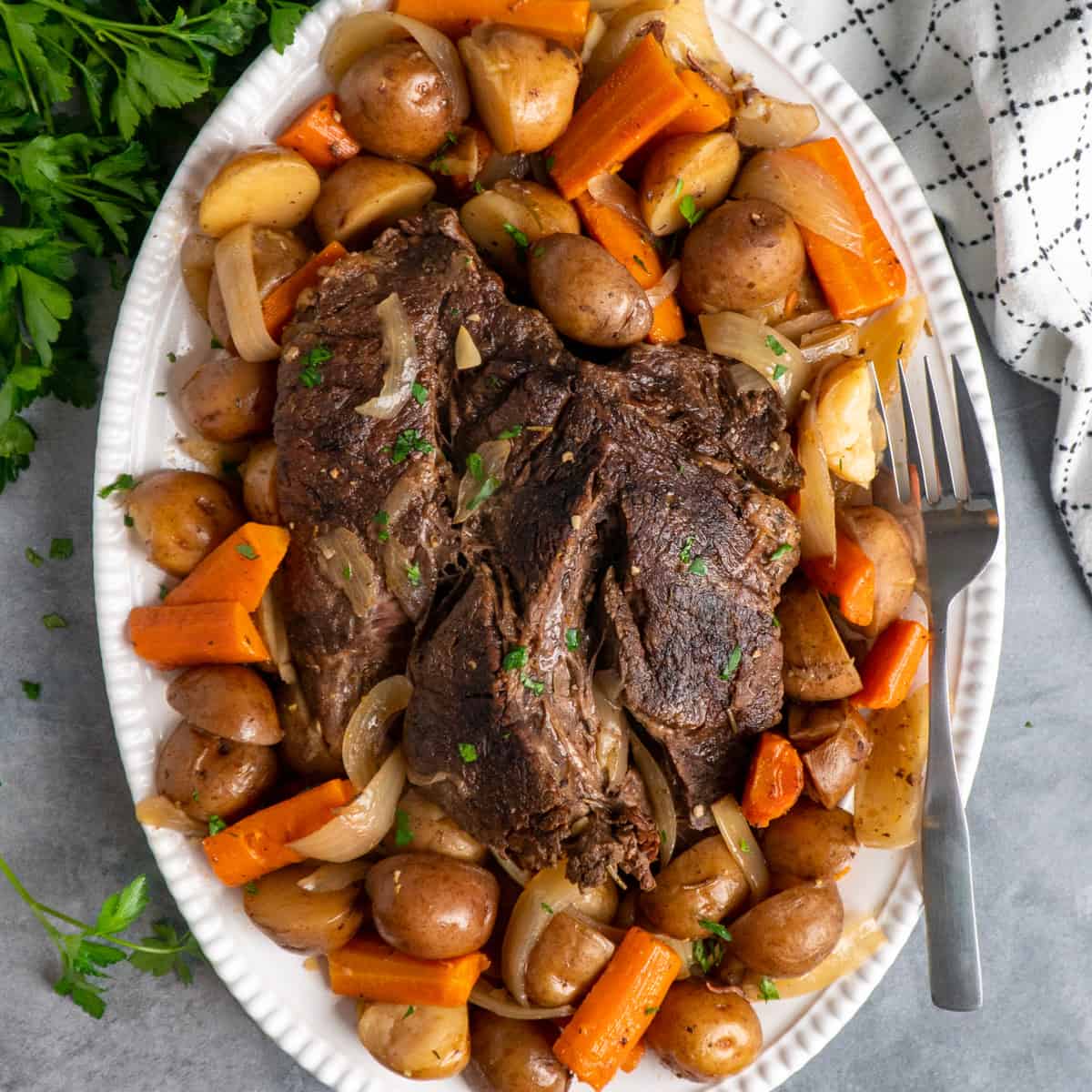 A pot roast on a plate with potatoes and carrots.