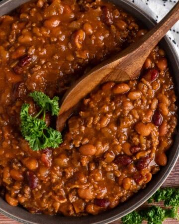 Slow cooker cowboy beans in a bowl with a wooden spoon.