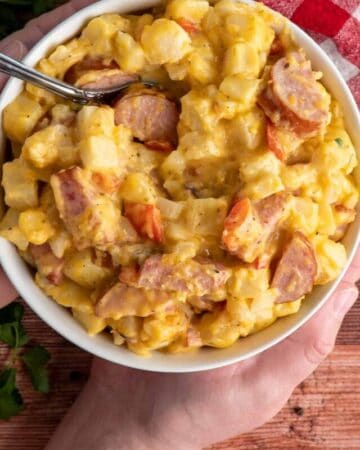 Hands holding a bowl of cheesy potatoes.