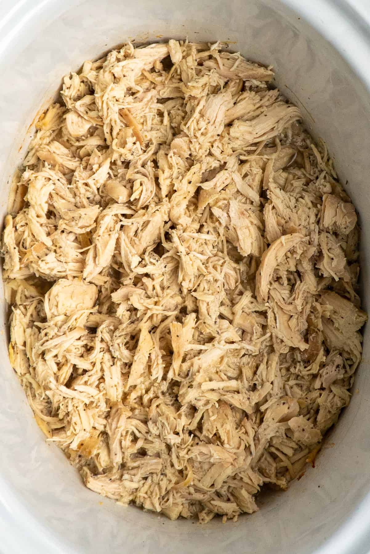 Overhead look at pulled chicken in a white crock pot.