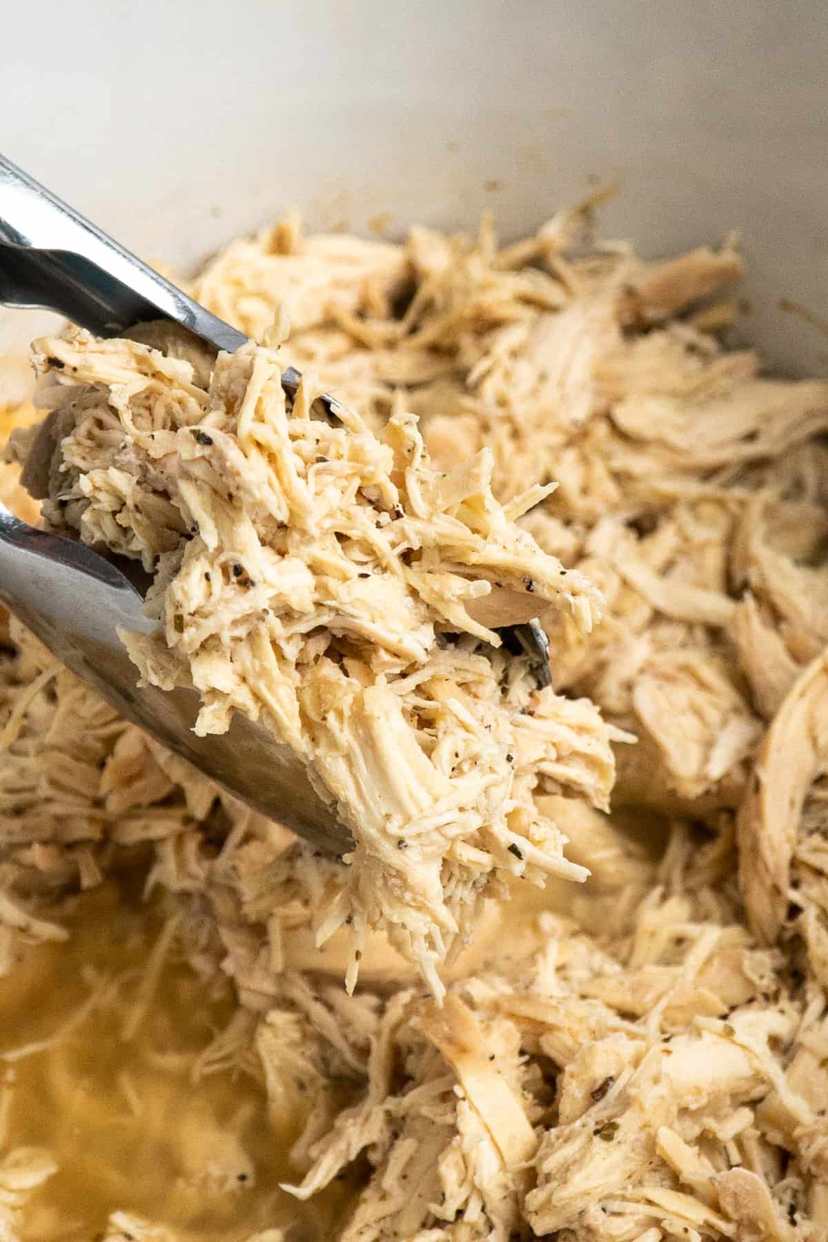 Tongs holding shredded chicken over a slow cooker.