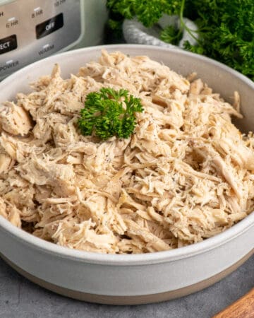 Crock Pot shredded chicken in a bowl garnished with parsley.