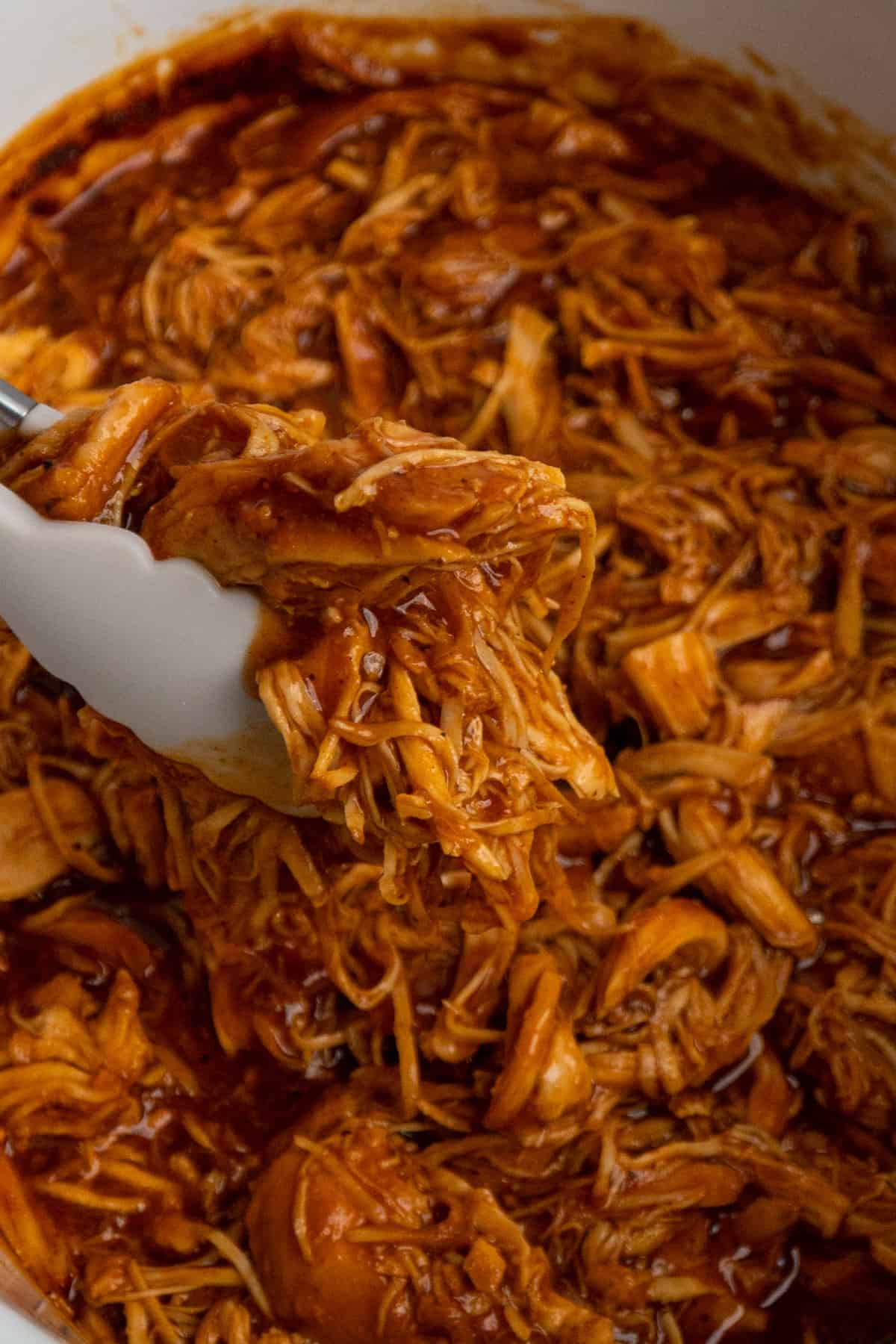 Tongs holding bbq pulled chicken over a crock pot.