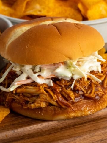 Close-up of crock pot pulled bbq chicken on a bun with cole slaw on top.