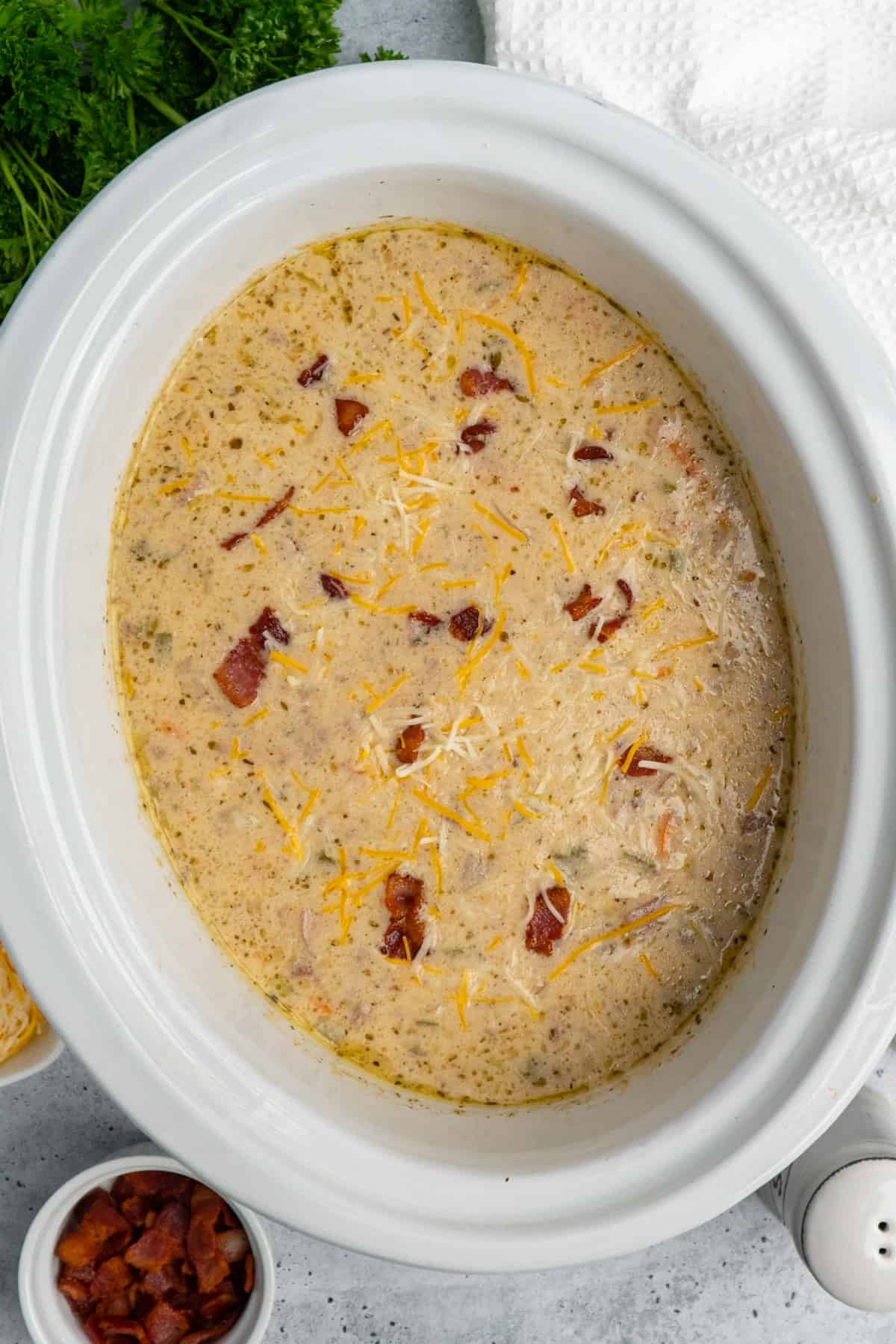 Overhead image of cheeseburger soup in a white slow cooker and garnished with cheese and bacon.