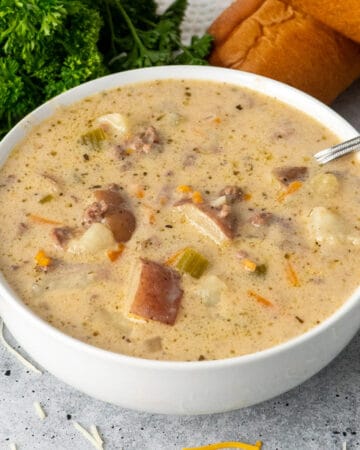 Crock Pot cheeseburger soup in a white bowl with bread in the background.