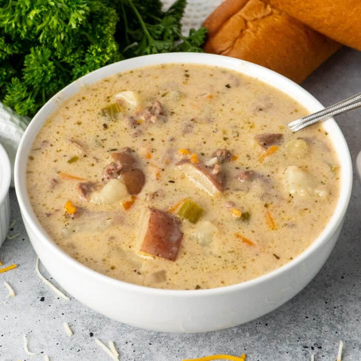 Crock Pot cheeseburger soup in a white bowl with bread in the background.