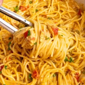 Close-up of tongs holding Crock Pot chicken spaghetti with Rotel.