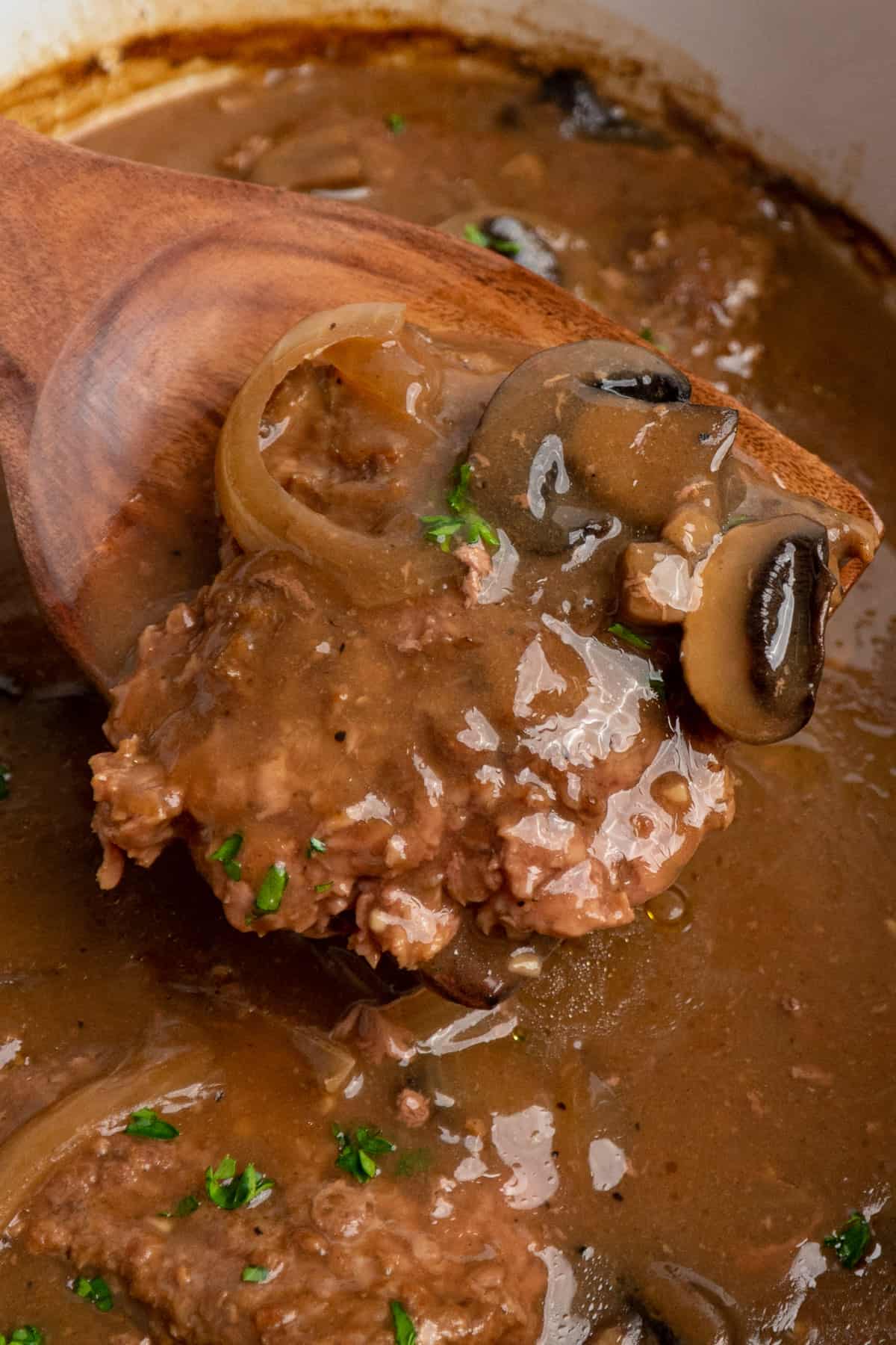 A wooden spoon holding a piece of cube steak with gravy and mushrooms.
