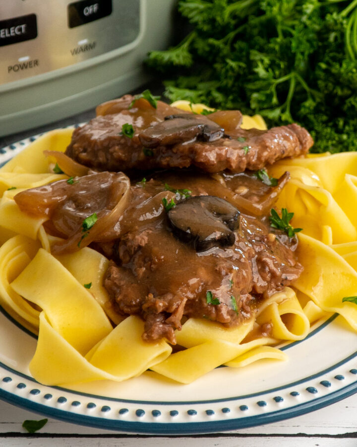 Crock pot cube steak over a plate of egg noodles.