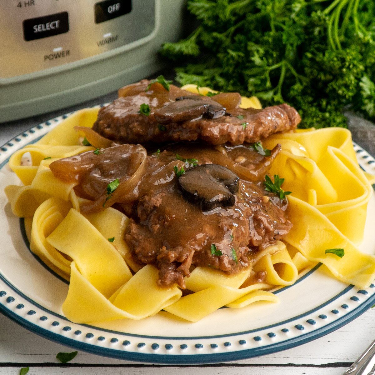 Crock pot cube steak on a plate of egg noodles.