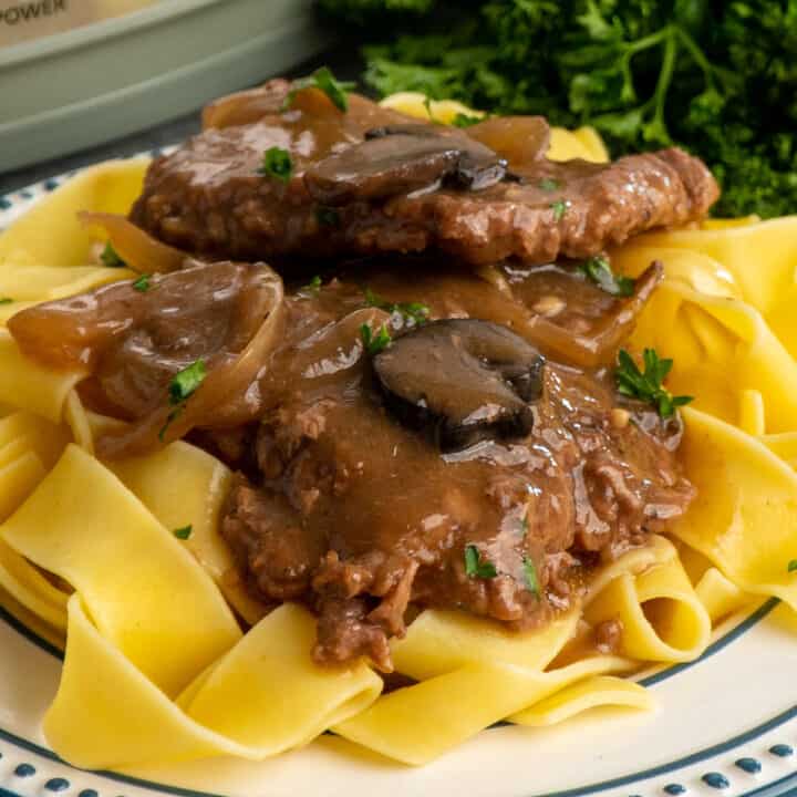 Crock pot cube steak over a plate of egg noodles.