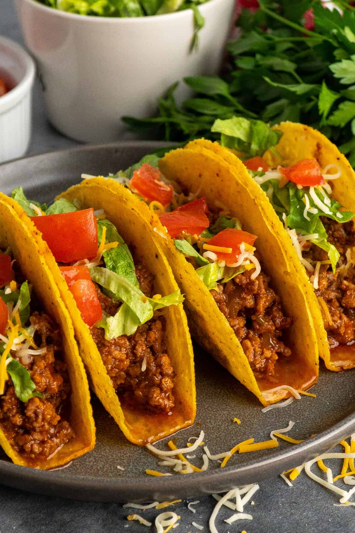 Four ground beef tacos in hard shells on a plate.