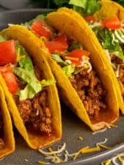 Four hard shell tacos with ground beef and garnished with tomatoes and lettuce.