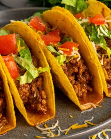 Four hard shell tacos with ground beef and garnished with tomatoes and lettuce.