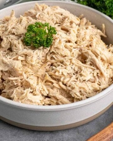 Crock Pot shredded chicken in a bowl garnished with parsley.