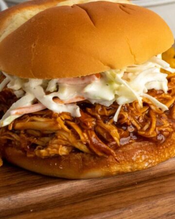 Close-up of crock pot pulled bbq chicken on a bun with cole slaw on top.