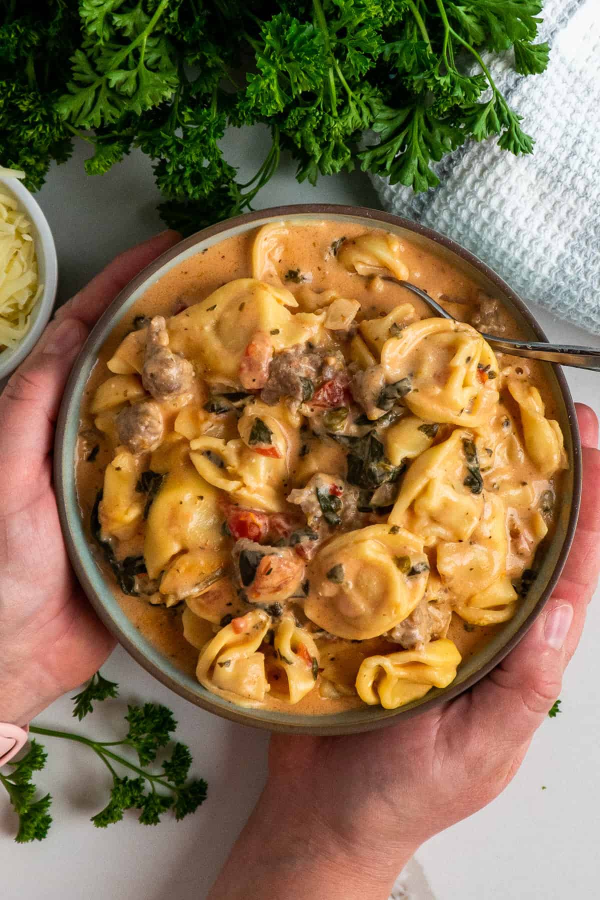 Hands holding a bowl of creamy crockpot tortellini.