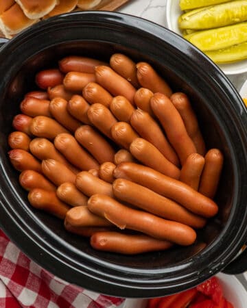 Cooked hot dogs in a black oval crock pot.