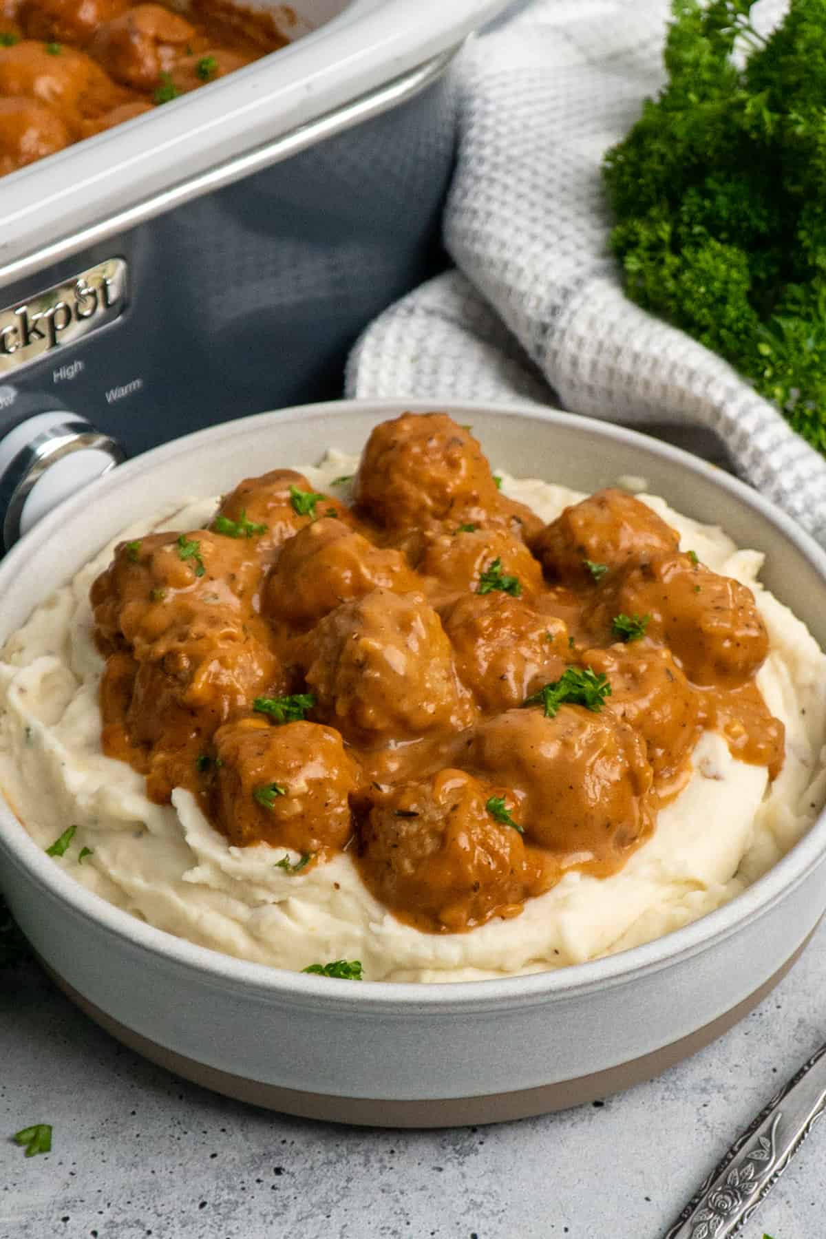Close up of meatballs over mashed potatoes with gravy on top.
