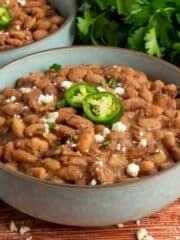 Crock pot pinto beans in a bowl garnished with jalapenos and cheese.