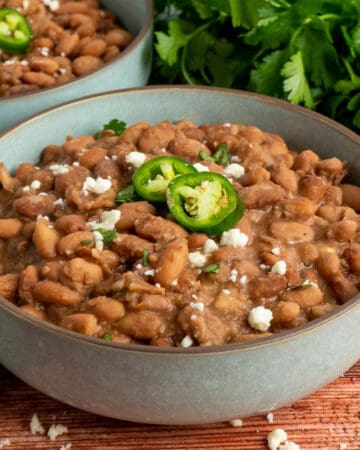Crock pot pinto beans in a bowl garnished with jalapenos and cheese.
