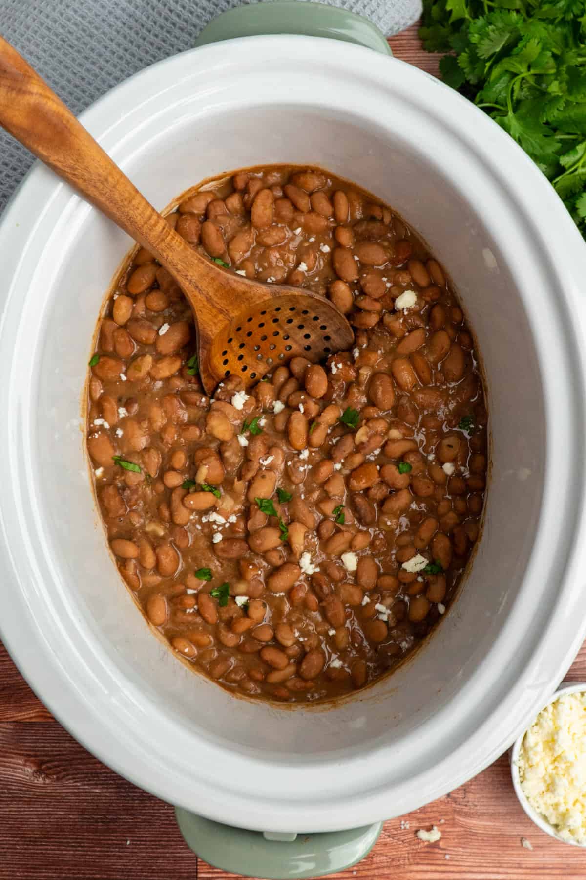 Overhead image of pinto beans in a crock pot with a wooden spoon.